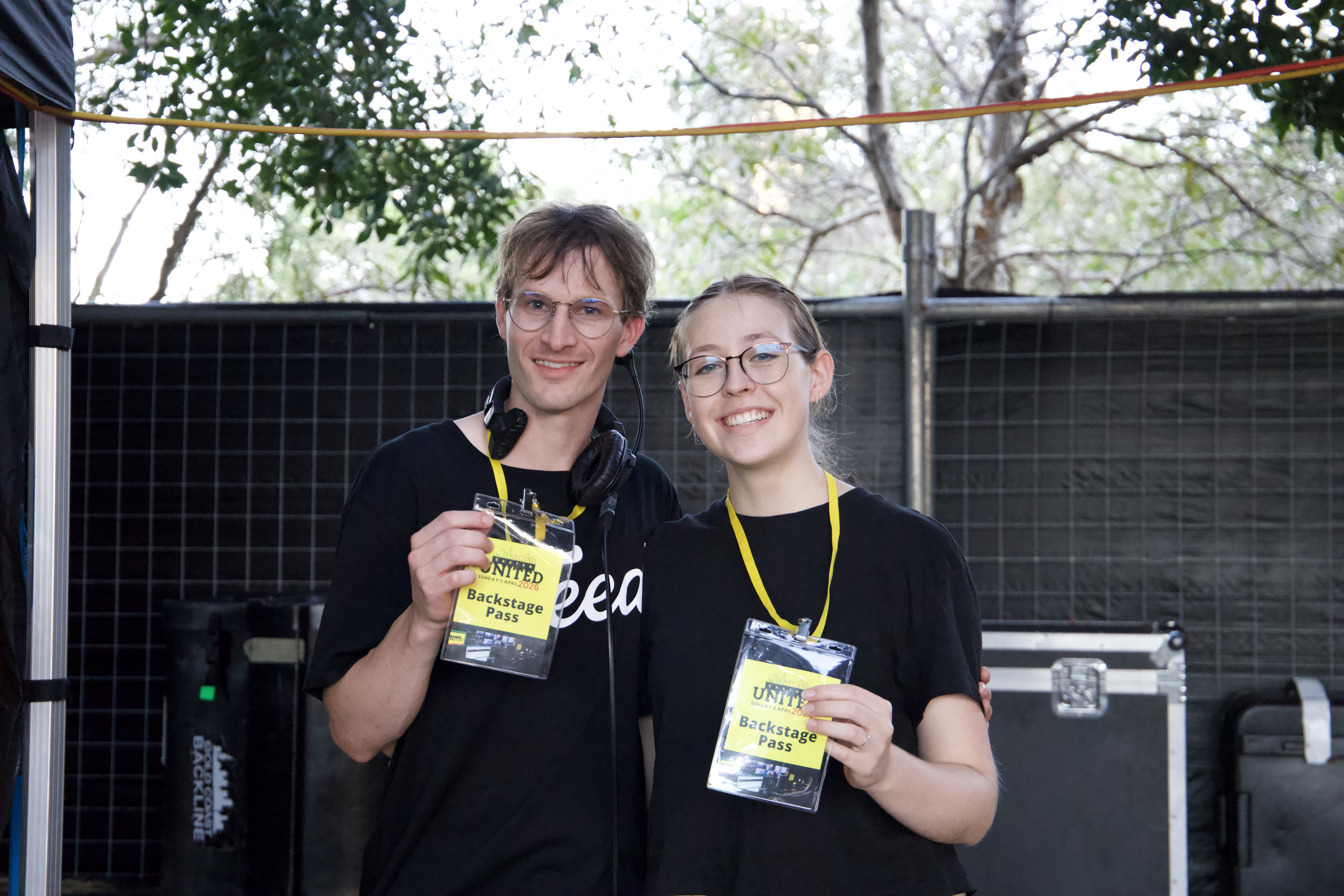 Two smiling Easter United crew members in black T-shirts holding up their yellow backstage passes